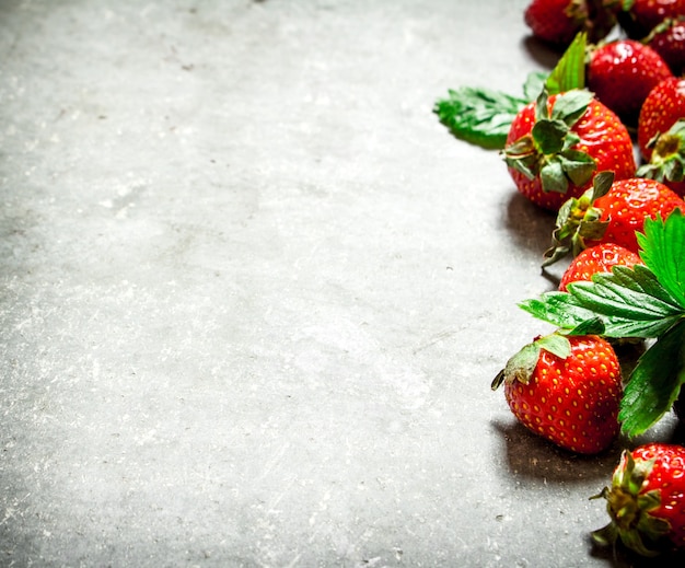 Strawberry with green leaves. On the stone table.