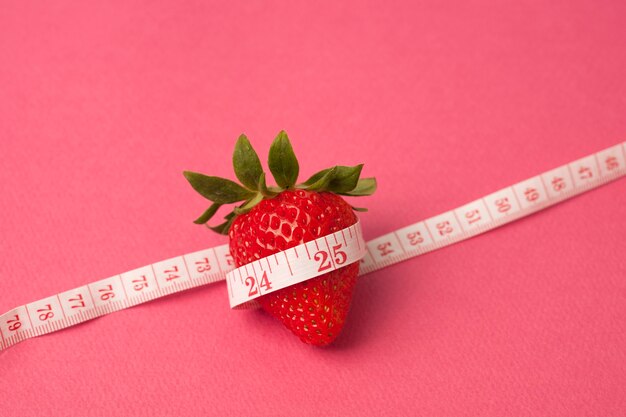 Strawberry with measure tape on pink background