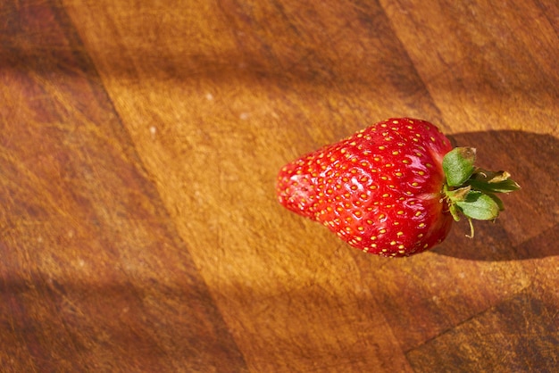 A strawberry with the top of it on a wooden table.