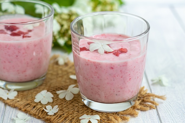 흰색 테이블에 딸기와 요구르트 스무디입니다. 엘더베리 꽃과 딸기로 장식되어 있습니다. 건강한 영양, 다이어트.