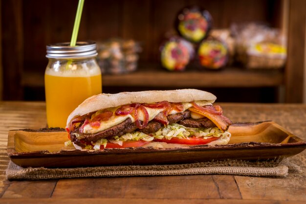 Сэндвич из говядины Ciabatta с сыром, беконом, помидорами и луком, апельсиновый сок в банку на деревенском наборе