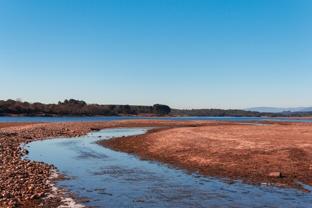 Stream flowing into a lake. Stones on the shore. Dry land. Complementary colors.