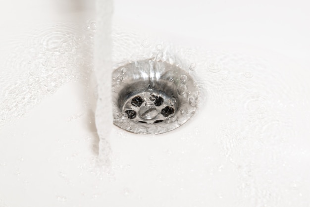 A stream of pure water flows into a white shell. Drain in a white sink, background, close-up.