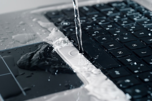 A stream of water pours on the laptop keyboard.