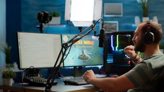 Streamer man talking with multiple players into headphones and winning video games competition. Professional gamer streaming online videogames with new graphics on powerful computer from gaming room