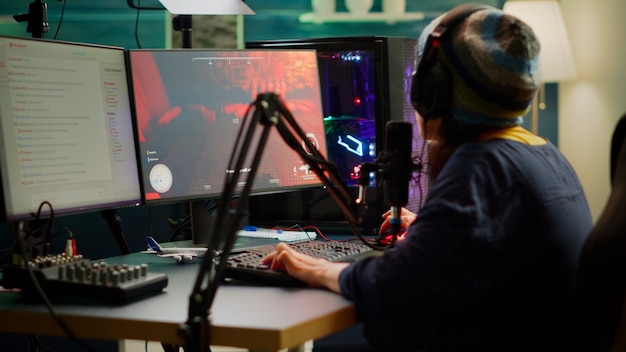 Streamer playing FPS videogames and talking with team mates on streaming open chat using professional microphone. Cyber performing in online tournament on RGB powerful computer in gaming sudio room