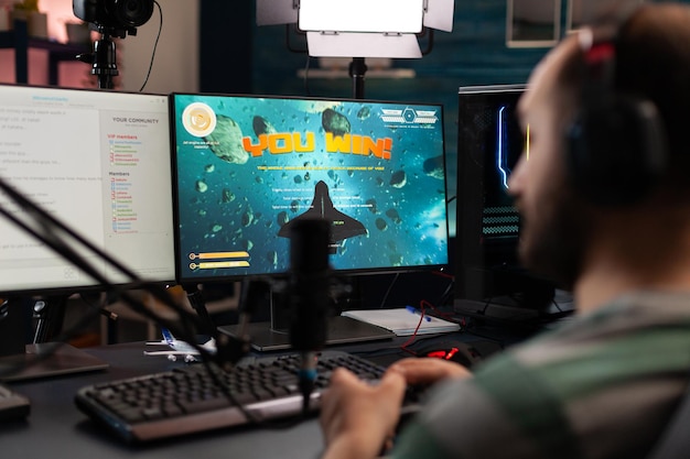 Streamer playing video games with controller on computer. Man live streaming gameplay and winning, using microphone and headphones while he talks to online chat on monitor. Gamer on stream