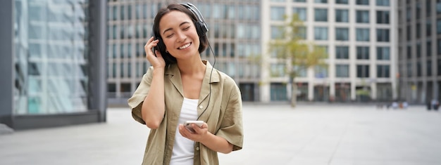 사진 스트리밍 서비스 개념 행복한 아시아 소녀는 휴대폰 선택을 통해 헤드폰을 끼고 음악을 듣습니다.
