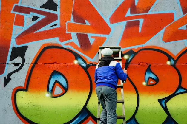 Street artist draws colorful and vibrant graffiti modern art concept with city guy artist applies bright graffiti on gray wall