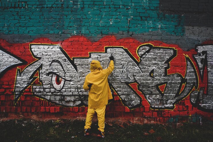 Street artist draws colorful and vibrant graffiti Modern art concept with city guy artist applies bright graffiti on gray wall