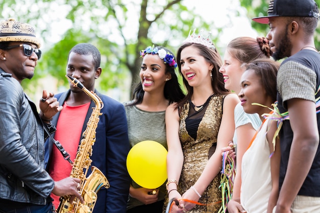 Street artist playing saxophone for multi-ethnic party group 