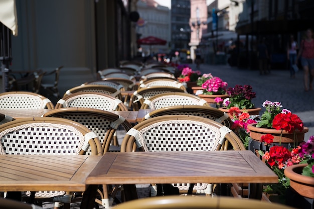 Street cafe or restaurant with tables, chairs and flowers in pots on sunny day outdoor on urban background. Food service, catering, dining, lounge, entertainment concept