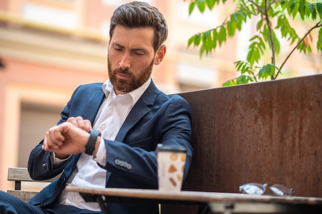 In the street cafe. Young man in a suit sitting in the street cafe and having coffee