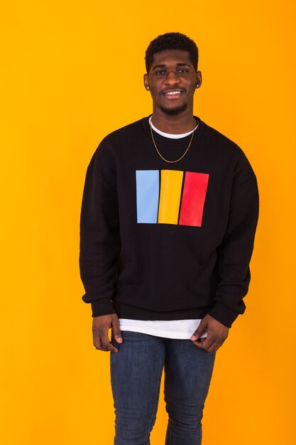 Street fashion concept - Studio shot of young handsome African man wearing sweatshirt against yellow