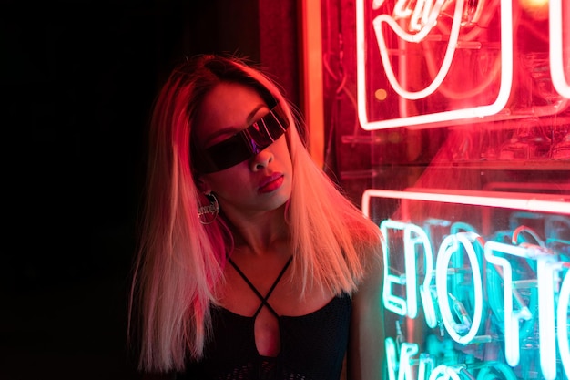 Street fashion young girl with sunglasses, neon light red blue, nightlife and trendy lifestyle