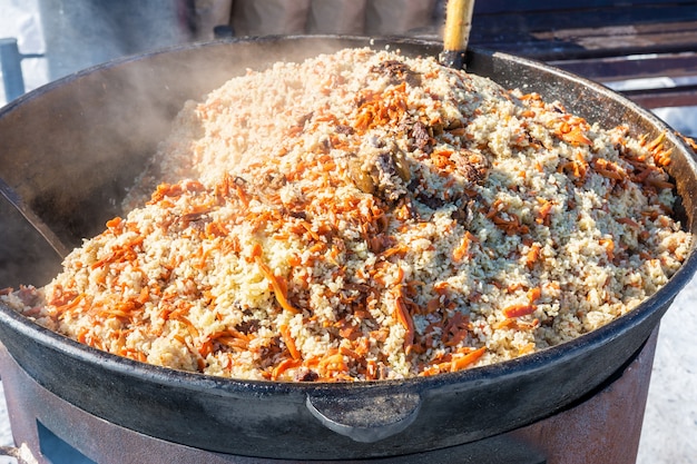 Street food Delicious pilaf is prepared in a large cauldron in the open air
