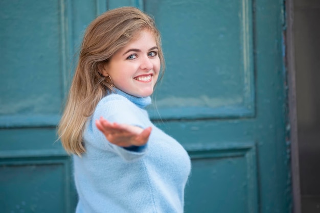 On the street a happy blonde girl in a blue knitted sweater stretches out her hand