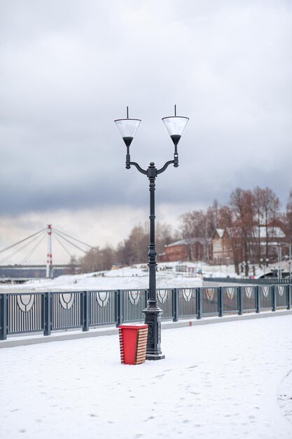 A street lamp in the snow with the red trash can in the foreground.