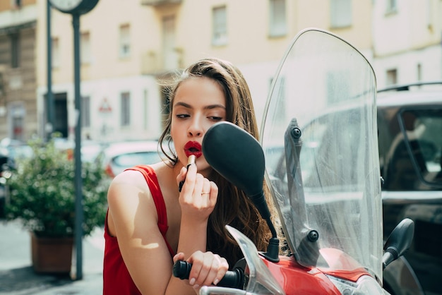 Street makeup. Sexy fashion girl with red lips put lipstick looking in a mirror of motorcycle.