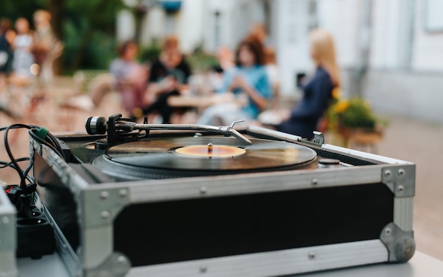 Primo piano del festival di musica di strada del giradischi in vinile e delle persone sedute nella caffetteria in bokeh messa a fuoco selettiva sullo stilo della cartuccia