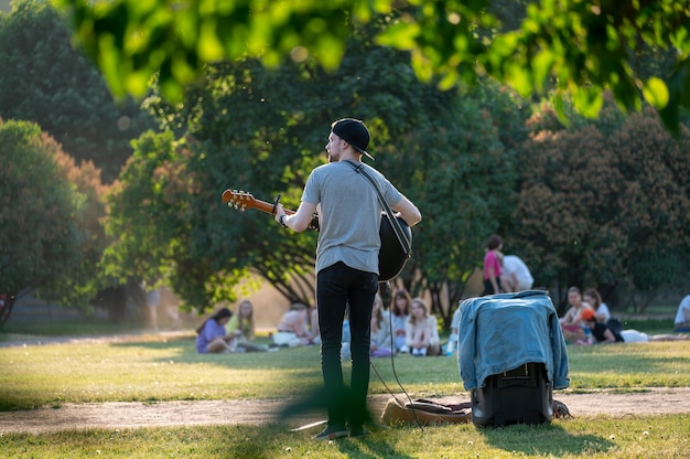거리의 음악가가 공원에서 기타를 연주합니다. 여름 녹색 공원, 록 음악가는 공원에서 무료 콘서트를 제공합니다. 기타와 함께 도시 공원에서 남자