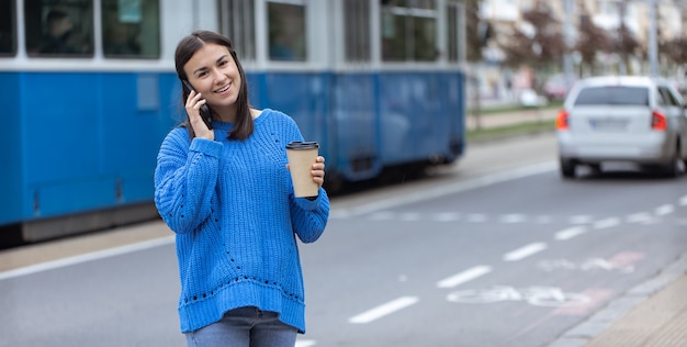 携帯電話を手に、コーヒーを飲みに行く若い女性のストリート写真。