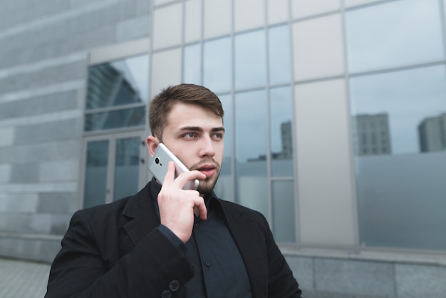 Street portrait of a beautiful man with a beard communicating on the phone against a modern building