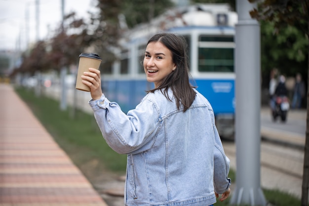 Street portrait of a cheerful young woman on a walk with coffee on a blurred background