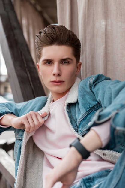 Street portrait good-looking young man with clean skin with stylish hairstyle in trendy blue denim jacket outdoors in city. Sexy guy fashion model in fashionable jeans clothes. Youth style.