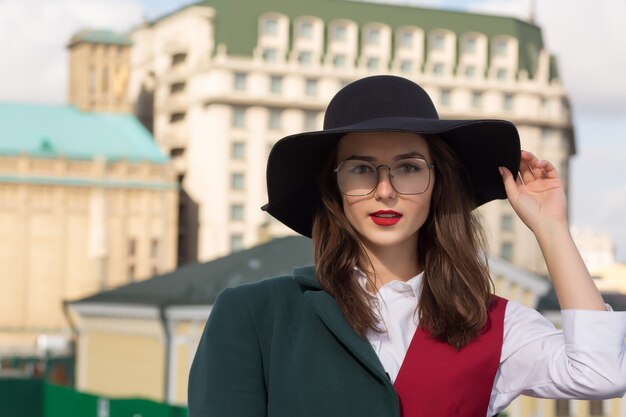 사진 도시에서 포즈를 취하는 멋진 젊은 여성의 거리 초상화. 세련된 모자와 안경을 쓴 여자