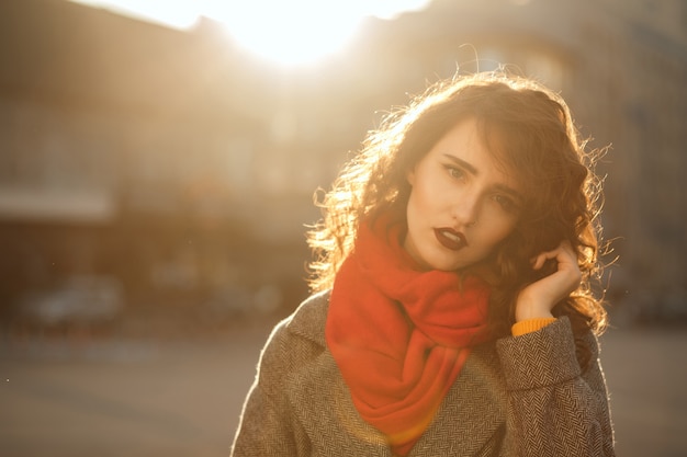 Street portrait of pretty brunette model with wavy hair posing in soft evening backlight. Space for text