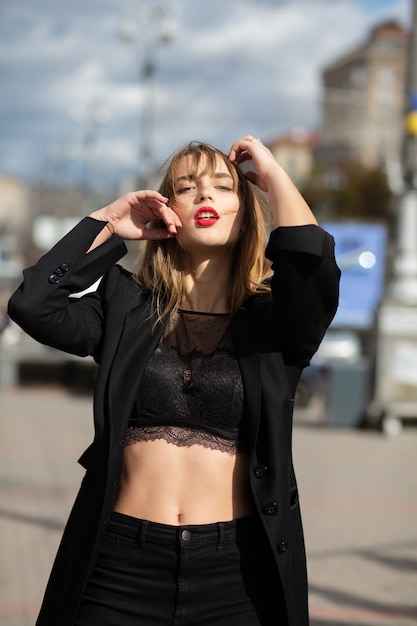 Street portrait of sexy woman with long hair wears lingerie and jacket posing at the street in Kyiv