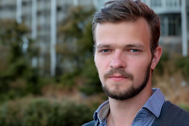 Street portrait of a young handsome man with a small beard and mustache in a vest on a warm summer day