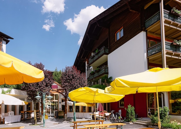 Уличный ресторан с зонтиками, столами и стульями в отеле и семейном курорте в Бад-Кляйнкирххайме в Каринтии, Австрия. Терраса кафе на тротуаре и архитектура здания с наружной. образ жизни
