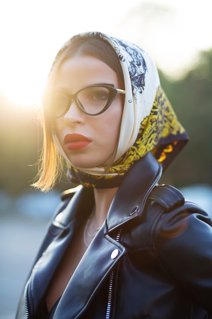 Street shot of fashionable brunette model with red lips wearing shawl and glasses