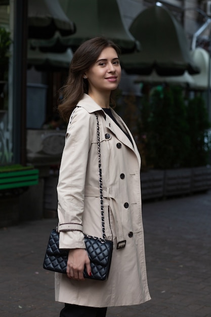 Street shot: smiling elegant woman with nude makeup wears beige spring coat. Space for text