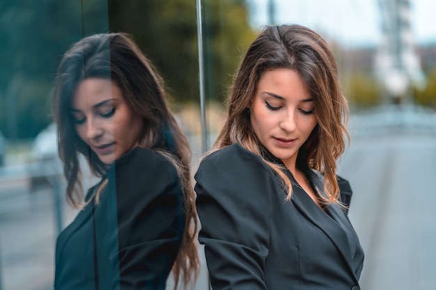 Street style, an enterprising young Caucasian woman entering the office to work in a black suit and heels. Reflected in the glass of the black glass building one spring morning