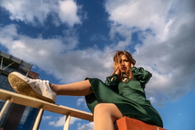 Foto ritratto di moda in stile strada di giovane ragazza dai capelli castani carina in un vestito verde sotto il cielo nuvoloso