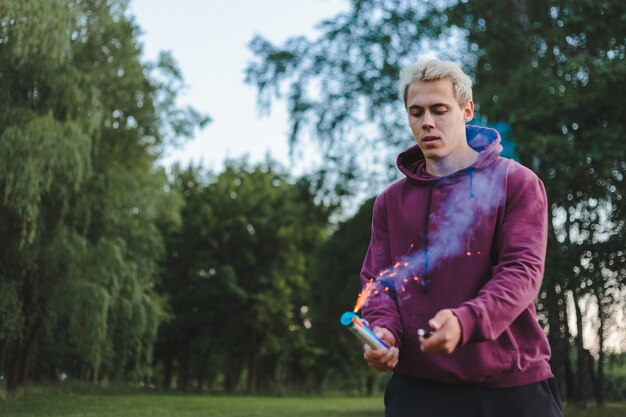 Street style man in hoodie hold hand flare with red smoke grenade bomb.