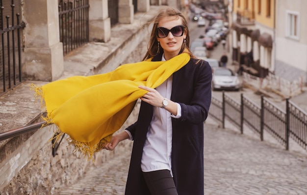 Street style photo of elegant fashionable woman wearing trendy clothes with scarf blowing in wind mo