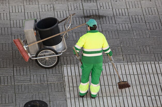 Street sweeper working on a sidewalk with her shovel trolley and broom