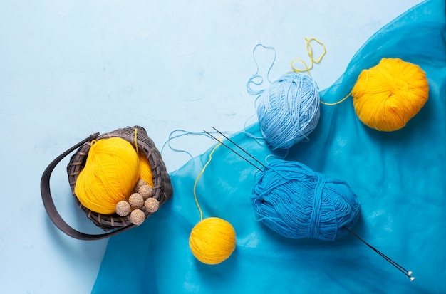 Strengen blauw, geel garen liggen op een lichtblauwe achtergrond, daarnaast staat een rieten mand.