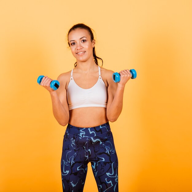 Strength and motivation. Full length of young and slim african woman in sports clothing exercising in studio against yellow background