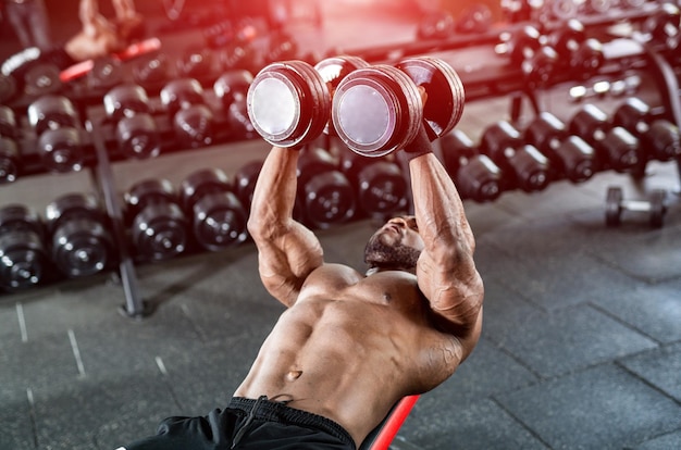 Strength workout Determined fit man exercising with dumbbells pumping muscles over dark gym background