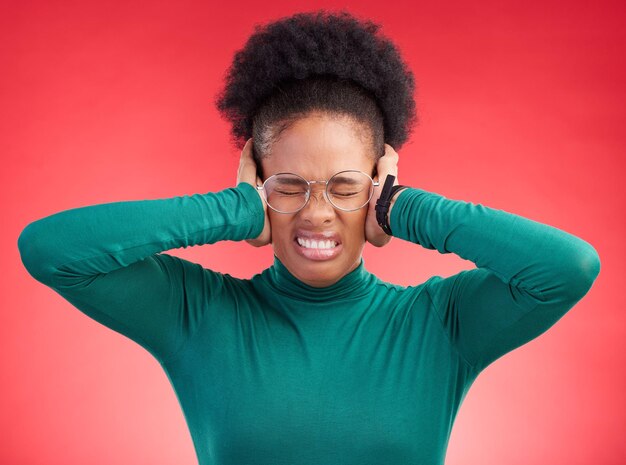 Stress headache and hands on ears of black woman in studio with noise complaint or frustration on red background Migraine anxiety and African female with vertigo brain fog or hearing loss crisis