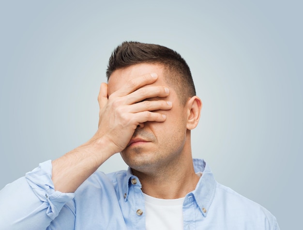 stress, headache, health care and people concept - unhappy man covering his eyes by hand over gray background