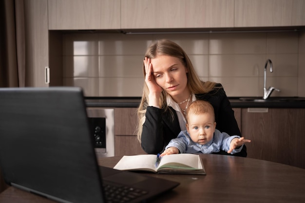 Stress on maternity leave A young woman with a baby in her arms suffers from a headache while working on a laptop in a home office a sick mother has difficulty multitasking