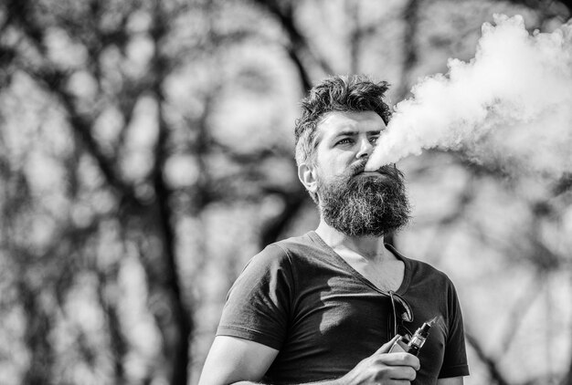 Stress relief concept Bearded man smoking vape Smoking electronic cigarette Man long beard relaxed with smoking habit Man with beard and mustache breathe out smoke White clouds of flavored smoke