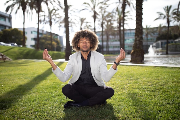 Концепция снятия стресса спокойный черный бизнесмен средних лет медитирует на открытом воздухе, практикует йогу сидя