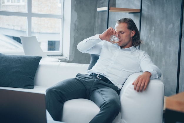 Stress relief. Young man sitting in a front of notebook and drinking whiskey